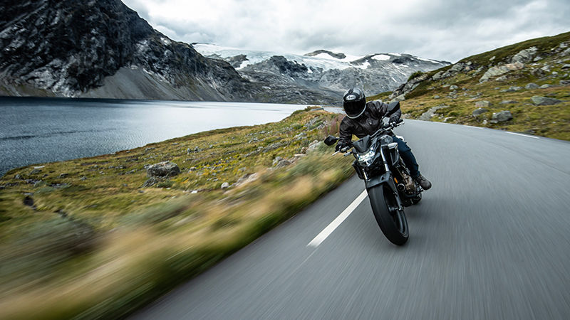 Motorcycle rider in a blacked out road helmet and jacket riding a back road by a lake.