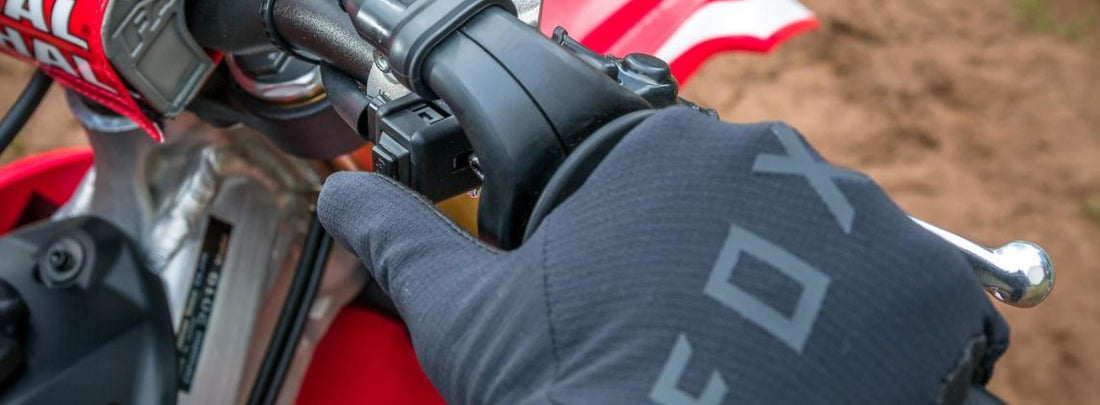 Hand on Honda CRF throttle wearing black Fox Motocross gloves