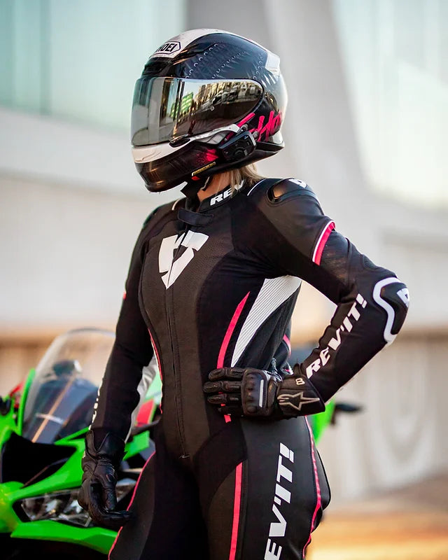 women wearing a motorcycle pink and black rev"it race suit with a black helmet on and alpinestar black gloves
