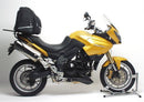 Three labeled items: Ventura EVO-12 bike-pack (black zippered bag), Adjustable Pack-Rack (black rear bike rack), and L-bracket with screws for Triumph Tiger 1050 (07-12). Text: "EVO-12 Bike-Pack Kit.