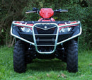 The Ventura Suzuki ATV LT-A 500 (13-18) in red, equipped with bull-bars, large black tires, and silver racks at both ends, is parked on the grass amidst green bushes and trees. It features a custom company logo on its side.