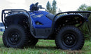 A blue Yamaha Kodiak 700 by Ventura, with large tires and black racks on front and back, is parked on grass. It features a logo on the side, with trees and a fence in the background.