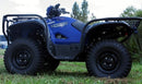 A Ventura Yamaha Grizzly 700 4x4 EPS (16 - >) ATV, in blue, is parked on grass amid green bushes. It features large rugged tires, a sturdy bull-bar, a front light, handlebar controls, and a protective front grille.