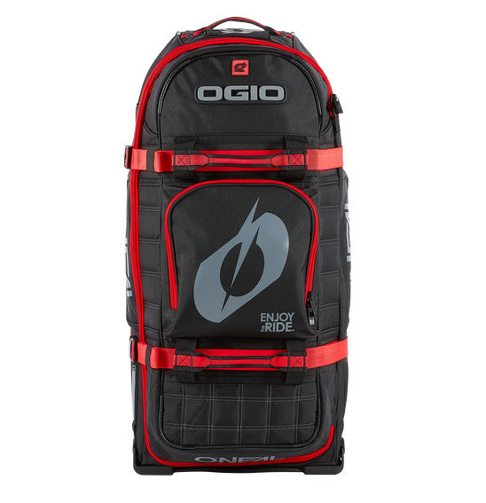 A large, black and red O'NEAL x OGIO RIG 9800 Gear Bag by ONEAL is standing upright. This travel bag is designed with multiple compartments, zippers, and adjustable straps. The SLED system ensures extra durability, while the OGIO logo is prominently displayed on the front alongside the text "ENJOY THE RIDE.