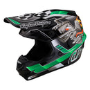 The Troy Lee Designs SE4 POLYACRYLITE HELMET W/MIPS CARB GREEN features bold graphics, a cartoon engine with flames, checkered flag pattern, “Troy Lee Designs” on the visor, and MIPS technology for enhanced safety.
