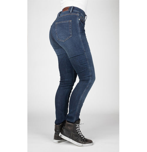 Illustration of a person wearing protective clothing, specifically the SALE - Bull-It Covert Blue Slim Jeans (AAA) - LADIES from BULL-IT. The image highlights features such as reinforcement in high-risk zones, abrasion-resistant materials, polyurethane armors, and moisture-wicking lining for superior motorcycle protection.