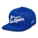 The Los Angeles Hat by Crown Kiwi Enterprises Limited is a blue cotton baseball cap with a flat bill, featuring "Los Angeles" in bold 3D embroidery and a stylized star design on the front.