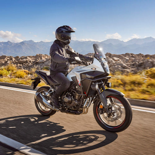 The Honda NX500, a sleek and modern motorcycle by Honda, showcases a silver and black color scheme with programmed fuel injection. It features a prominent windshield, angular design elements, and alloy wheels. The side profile accentuates its sporty and aerodynamic build.