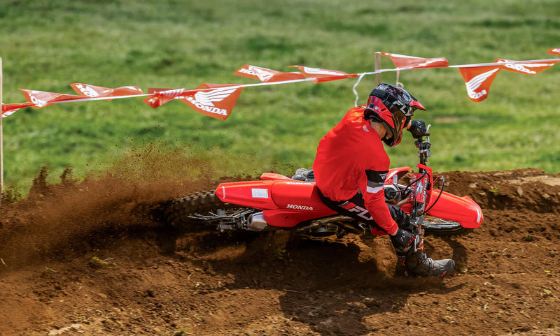 Side view of a red 2025 Honda CRF250R motocross dirt bike with black tires, visible spokes, and a silver exhaust pipe. The bike features the Honda logo on the seat and a number graphic on the side panel. Equipped with HRC Launch Control and a sturdy frame, it’s designed for optimal off-road use.