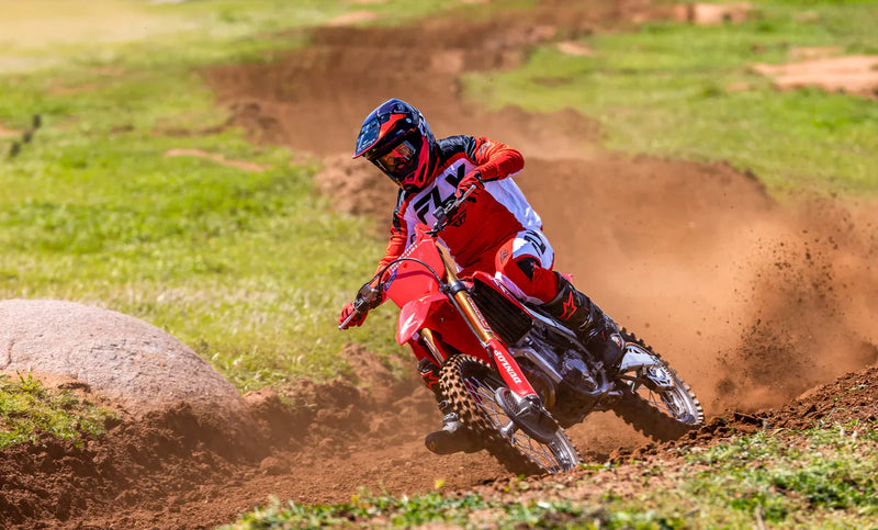 Side view of a red 2025 Honda CRF250R motocross dirt bike with black tires, visible spokes, and a silver exhaust pipe. The bike features the Honda logo on the seat and a number graphic on the side panel. Equipped with HRC Launch Control and a sturdy frame, it’s designed for optimal off-road use.