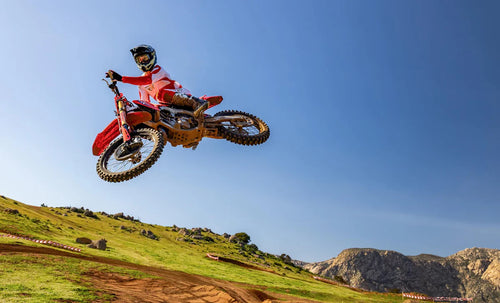 Side view of a red 2025 Honda CRF250R motocross dirt bike with black tires, visible spokes, and a silver exhaust pipe. The bike features the Honda logo on the seat and a number graphic on the side panel. Equipped with HRC Launch Control and a sturdy frame, it’s designed for optimal off-road use.