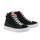 The Stella Stated Podium Shoes by Crown Kiwi Enterprises Limited are black high-top skate shoes designed with abrasion-resistant materials, featuring white soles and laces. The tongue includes a red pull tab for easy access. For a stylish display, the left shoe is positioned at an angle, slightly in front of the right.
