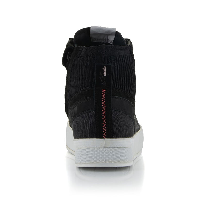 The Stella Stated Podium Shoes by Crown Kiwi Enterprises Limited are black high-top skate shoes designed with abrasion-resistant materials, featuring white soles and laces. The tongue includes a red pull tab for easy access. For a stylish display, the left shoe is positioned at an angle, slightly in front of the right.