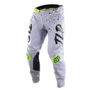 The Troy Lee Designs GP Pro Pant Partical Fog/Charcoal features black lettering, neon yellow accents, and a splatter design, made from durable 600D polyester with stretch panels for comfort, shown upright on a white background.