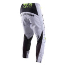 The Troy Lee Designs GP Pro Pant Partical Fog/Charcoal features black lettering, neon yellow accents, and a splatter design, made from durable 600D polyester with stretch panels for comfort, shown upright on a white background.