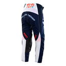 The Troy Lee Designs YOUTH GP PRO PANT PARTICAL NAVY / ORANGE features navy blue with orange accents, white and red details, TLD branding on one leg, heat and abrasion resistant panels, and a belt closure—displayed standing upright.