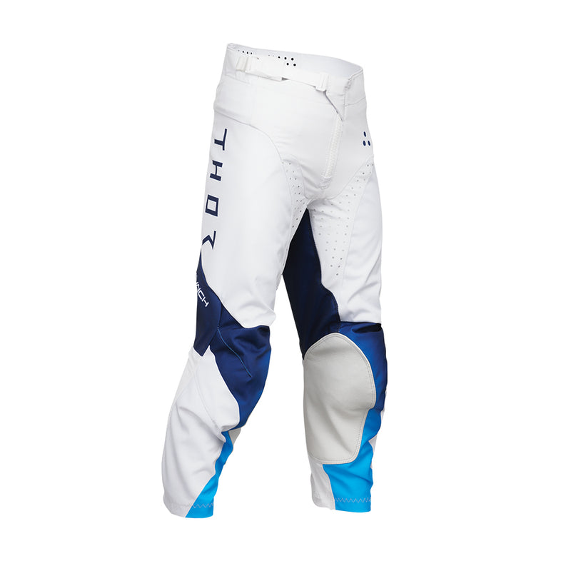 The THOR MX Launch Youth Storm White pants are crafted with durability in mind, showcasing a white fabric enhanced with blue and black accents. They feature padded knees for protection, a flexible and moisture-wicking design, and proudly display the brand name "Thor" printed vertically on the side.