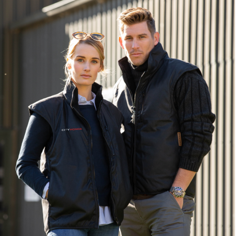 The Styx Mill X City Honda Oilskin Vest by STYX MILL is a sleeveless black vest with a zip front, chest zip pocket, and "CITY HONDA" embroidered in white and red on the left chest.