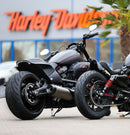 Two black Harley-Davidson motorcycles, sporting robust Metzeler CRUISETEC - Performance Cruiser tires by METZELER, are parked in front of a Harley-Davidson dealership. The image showcases the motorcycles' large rear tires, sleek design, and a hint of urban surroundings with the dealership's branded sign in the background.