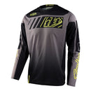 The Troy Lee Designs GP Jersey Icon Black/Gray is a long-sleeved motocross jersey with yellow accents, made from breathable material. It features bold geometric graphics and stylized branding on the chest, sleeves, and hem.