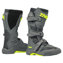 A pair of THOR MX Blitz XR youth boots in gray and charcoal, accented with neon yellow. Made from synthetic materials, they feature multiple adjustable straps and textured soles. One boot is positioned upright while the other is angled to display its back and side profile. Both boots prominently showcase the Thor logo.