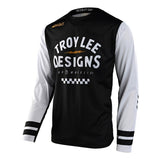 The Troy Lee Designs SCOUT GP JERSEY RIDE ON BLACK / WHITE is a long-sleeve cycling jersey made from breathable TLD Dura Knit Fabric, featuring a black body, white sleeves, graphic accents, striped cuffs, and bold branding across the chest.