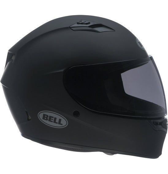 A Bell QUALIFIER Matte Black full-face motorcycle helmet is shown from a side angle, featuring an aerodynamic design with a smooth matte finish and a clear visor. The helmet includes a top vent for airflow, the "Bell" logo on the side, and Multi-Density EPS Liner for enhanced safety.