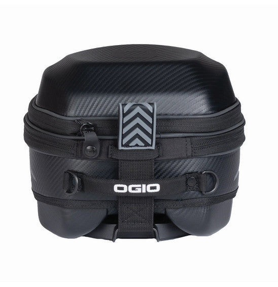 An open view of the OGIO TB1 TAIL BAG 14L - Ram Mount, a small black rectangular hardshell case, reveals an interior lined with soft padded material for protection. The exterior showcases its textured finish and two metal rivets on the front, with a zipper running along the edge.