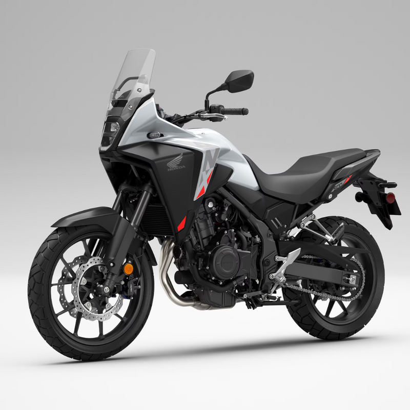 The Honda NX500, a sleek and modern motorcycle by Honda, showcases a silver and black color scheme with programmed fuel injection. It features a prominent windshield, angular design elements, and alloy wheels. The side profile accentuates its sporty and aerodynamic build.