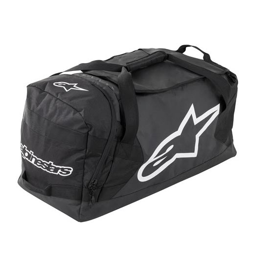 The ALPINESTARS Goanna Duffle Moto Bag is black with bold white logos, carrying handles, a shoulder strap, and a dedicated boots compartment for organized storage.