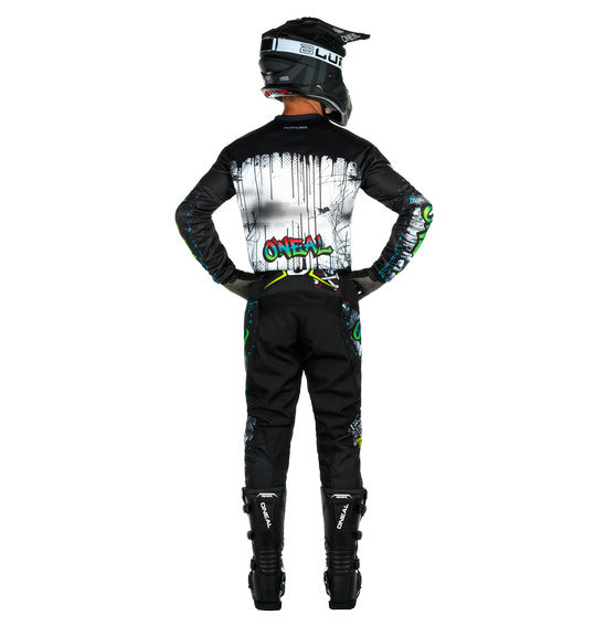 A person wearing a black and multi-colored O'Neal 2025 Youth ELEMENT Rancid Jersey, complete with helmet, gloves, pants, and boots stands with their back to the camera. The riding gear features breathable material adorned with various graphics and logos, the most prominent being "ONEAL Element" in colorful graffiti style on the back.