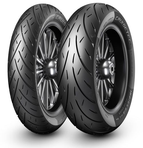 Two black Harley-Davidson motorcycles, sporting robust Metzeler CRUISETEC - Performance Cruiser tires by METZELER, are parked in front of a Harley-Davidson dealership. The image showcases the motorcycles' large rear tires, sleek design, and a hint of urban surroundings with the dealership's branded sign in the background.