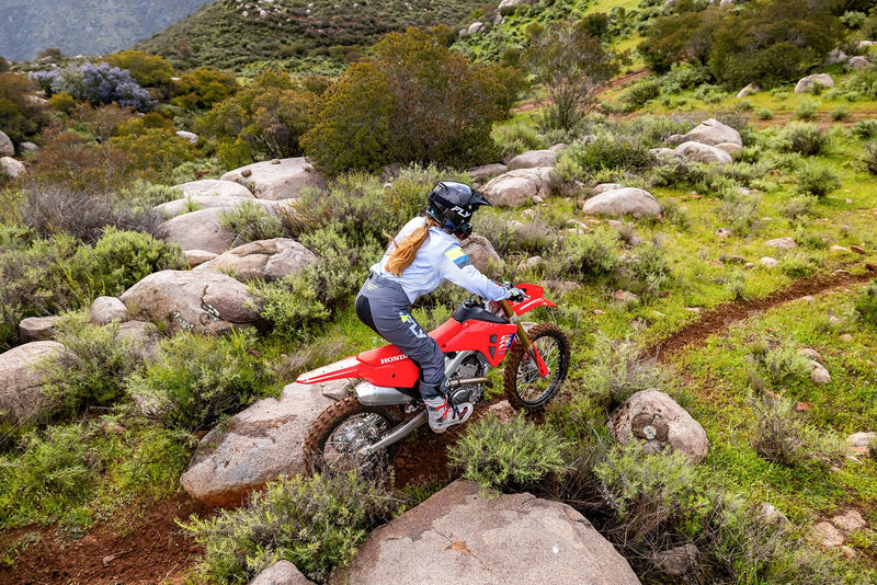 The 2025 Honda CRF250RX is a red off-road bike featuring a sturdy frame, knobby tires, and a black seat. It includes front and rear suspension with visible springs and displays prominent "Honda" branding on the side. The motorcycle is presented against a plain backdrop.