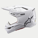 The ALPINESTARS Supertech S-M10 Solid White is a sleek, aerodynamic full-face motocross helmet with ventilation openings and angular contours. A black logo on the side enhances its modern style against a light gray background.