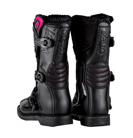 The O'Neal Women's RIDER PRO Boot in Black/Pink features the brand name "ONEAL" prominently and boasts multiple buckles along with rugged soles that have "ONEAL" embossed on the bottom. One boot stands upright while the other is tilted to display the sole, making them perfect for any motocross enthusiast.