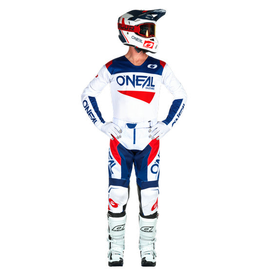 A person wearing the ONEAL O'Neal 2025 HARDWEAR AIR Slam Pant in White/Blue/Red, designed with vented construction and ergonomic fit, stands hands on hips facing away from the camera against a white background.