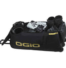 A large black OGIO Dozer Gearbag with a telescopic handle. It features the OGIO logo in yellow on the top flap and side. The bag has multiple zippered compartments, including a quilted front pocket and boot compartment for gear protection, and three sturdy wheels for easy transport.
