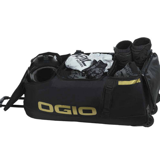 A large black OGIO Dozer Gearbag with a telescopic handle. It features the OGIO logo in yellow on the top flap and side. The bag has multiple zippered compartments, including a quilted front pocket and boot compartment for gear protection, and three sturdy wheels for easy transport.
