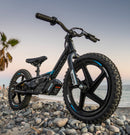 The STACYC 16eDRIVE Brushless - Electric Balance Bike by STACYC is a black model equipped with 16” composite wheels and a high-output brushless motor. It features large tires, a low seat, and adjustable handlebars, highlighted in blue and white with brand markings on the frame. Its compact, minimalist design incorporates a lithium-ion battery.