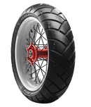 Close-up of a motorcycle wheel against a black background. The tire, an "Avon Trailrider" by Avon Tyres, is black with a white sidewall. It features a white rim, a red hub with black spokes, and has a distinct tread pattern.
