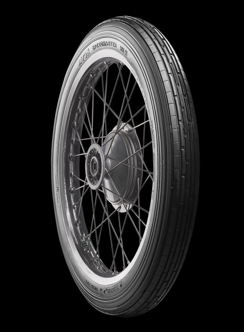 A black Avon Vintage and Classic Tire by Avon Tyres with a shiny silver rim shows a classic tread of thin parallel grooves on its circumference, set against a plain white background.