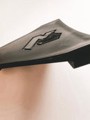 Close-up of the Rabaconda Bead Break Cover for Street Bike Tyre Changer by Rabaconda, featuring a sleek black plastic design with angular lines and a raised geometric pattern on a white background. Its surface is smooth and reflective.