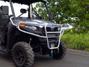 A Ventura CF Moto CF Moto U Force 600 (22 ->), a black off-road utility vehicle, is parked near greenery. It features large tires, bull-bars, a front metal guard, and an open cabin that reveals the driver's seat. The sky is partly cloudy with trees in the background.