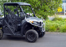 A Ventura CF Moto CF Moto U Force 600 (22 ->), a black off-road utility vehicle, is parked near greenery. It features large tires, bull-bars, a front metal guard, and an open cabin that reveals the driver's seat. The sky is partly cloudy with trees in the background.