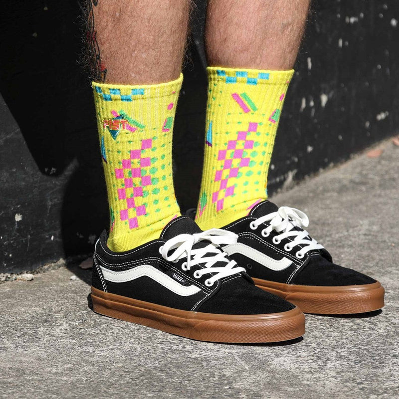 A pair of AEROBIX FLUORO YELLOW SOCKS with various colorful patterns, including pink and green geometric shapes, checkerboard designs, and zigzag lines. Crafted from super soft cotton, they feature targeted arch compression for added support and the brand name "FIST" near the top. The toes are solid yellow.