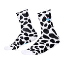 The DALMATION SOCK by FIST is a pair of white crew socks adorned with black irregular spot patterns reminiscent of cow print. These ultra-soft cotton socks also showcase a small colorful graphic near the top and offer targeted arch compression for enhanced support. They are shown against a white background.