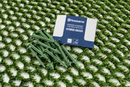 A pack of Husqvarna Automower® Hybrid Grass with green stakes is placed on top of an artificial grass mesh.