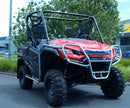 A Ventura Honda Pioneer 1000-3P (22 ->), a red off-road vehicle, is parked on a street. It boasts a sturdy metal frame, bull-bars, and large rugged tires. Its open cabin complements the greenery and industrial-style buildings seen in the background.