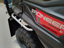 A Ventura Honda Pioneer 1000-5P in red and black, featuring roll bars and rugged tires, is parked on a paved area before a large industrial building with a corrugated metal facade.