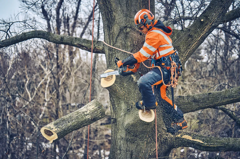 The Husqvarna Climbing Harness by Husqvarna is a black and orange industrial safety harness featuring padded hips and adjustable leg loops. Designed with multiple blue loops and straps, it is ideal for tree climbing or high-altitude work. This comfortable harness includes reinforced stitching and durable materials to ensure secure support.